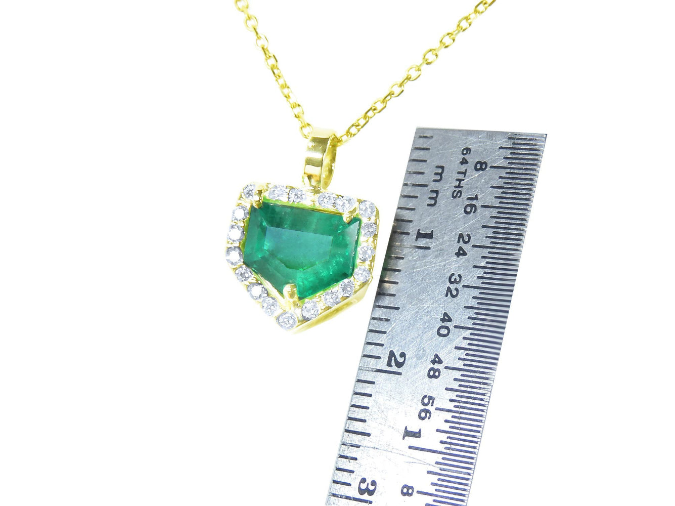 Gold necklace with a Muzo mine emerald pendant next to a ruler for size reference on a white background