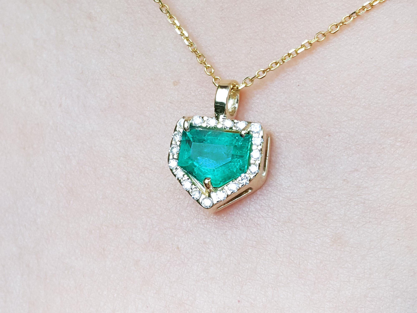 Gold necklace with a heart-shaped emerald pendant on a light pink background.