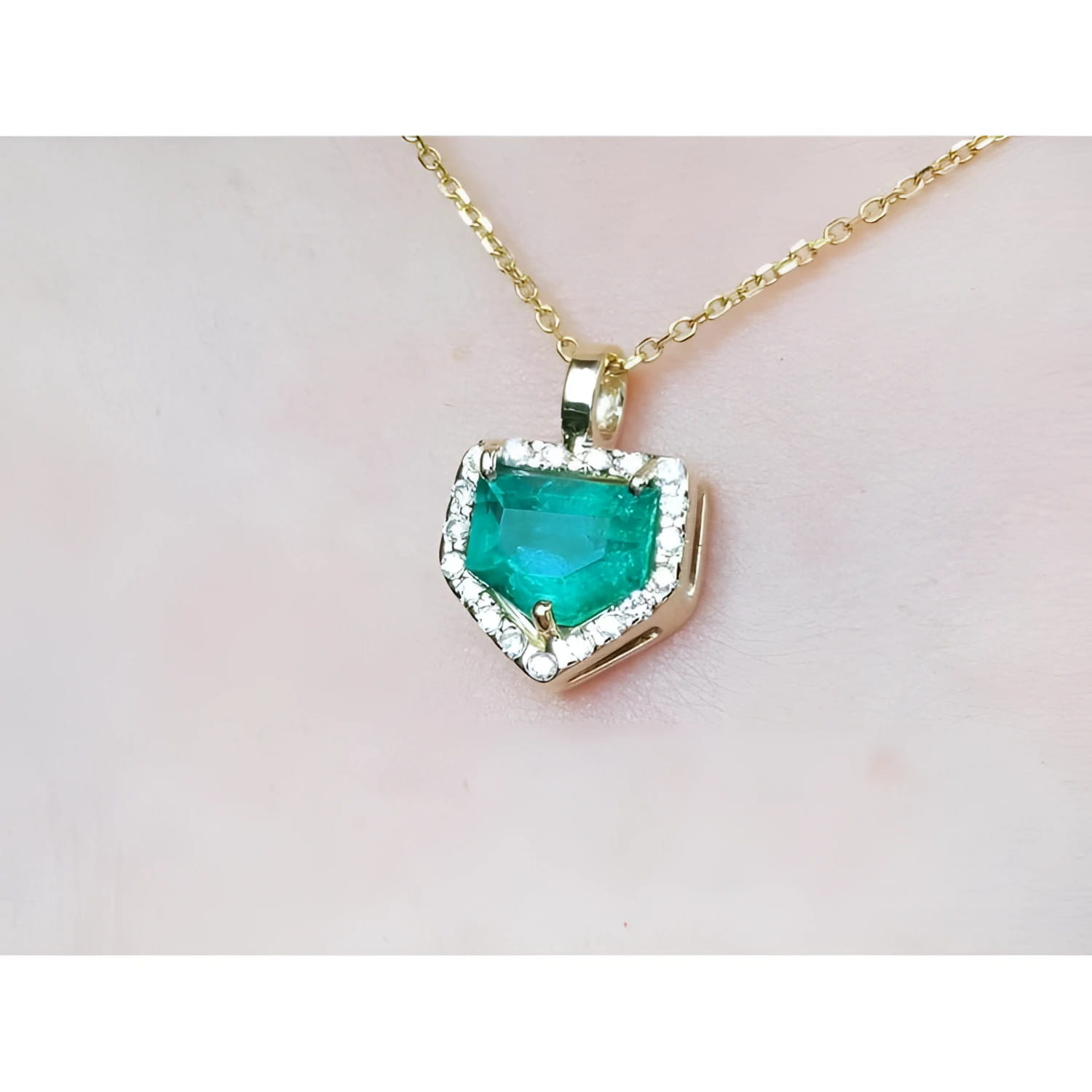 Gold necklace with a heart-shaped emerald pendant on a light pink background.