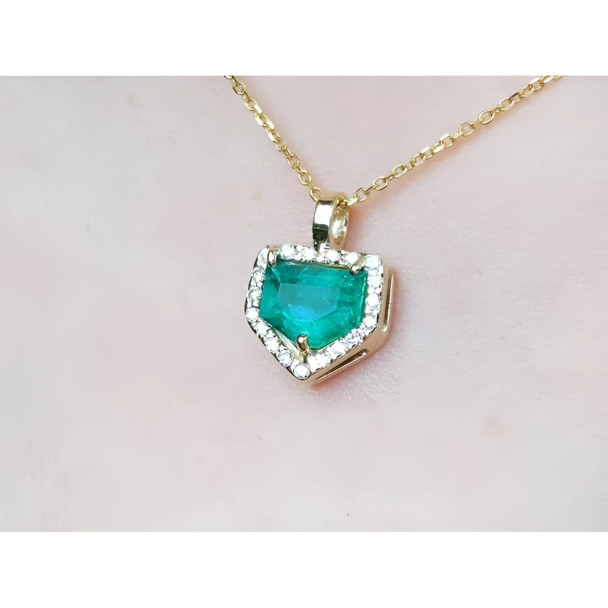 Gold necklace with a heart-shaped emerald pendant on a light pink background.