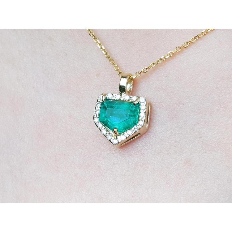 Gold necklace with a heart-shaped emerald pendant on a light pink background.