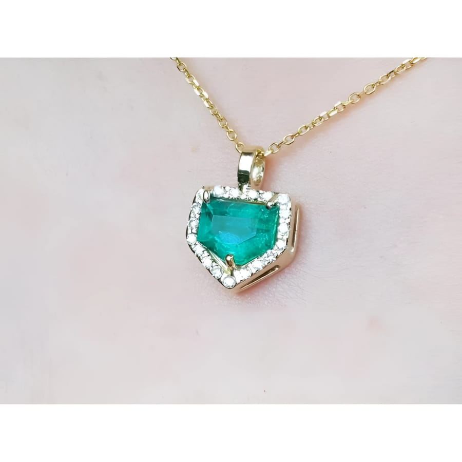 Gold necklace with a heart-shaped emerald pendant on a light pink background.