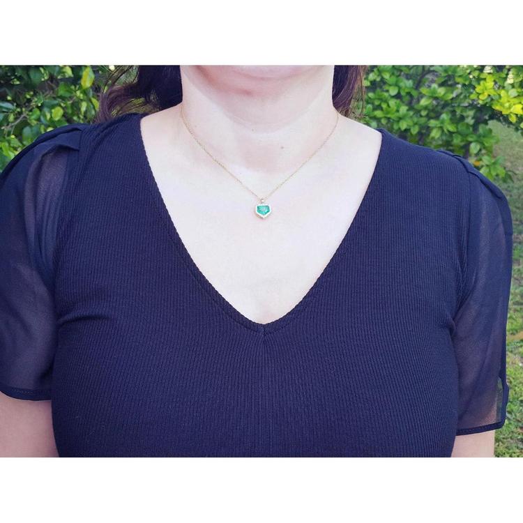 14K gold pendant with a vibrant Colombian emerald and diamond halo, worn on a woman's neck.