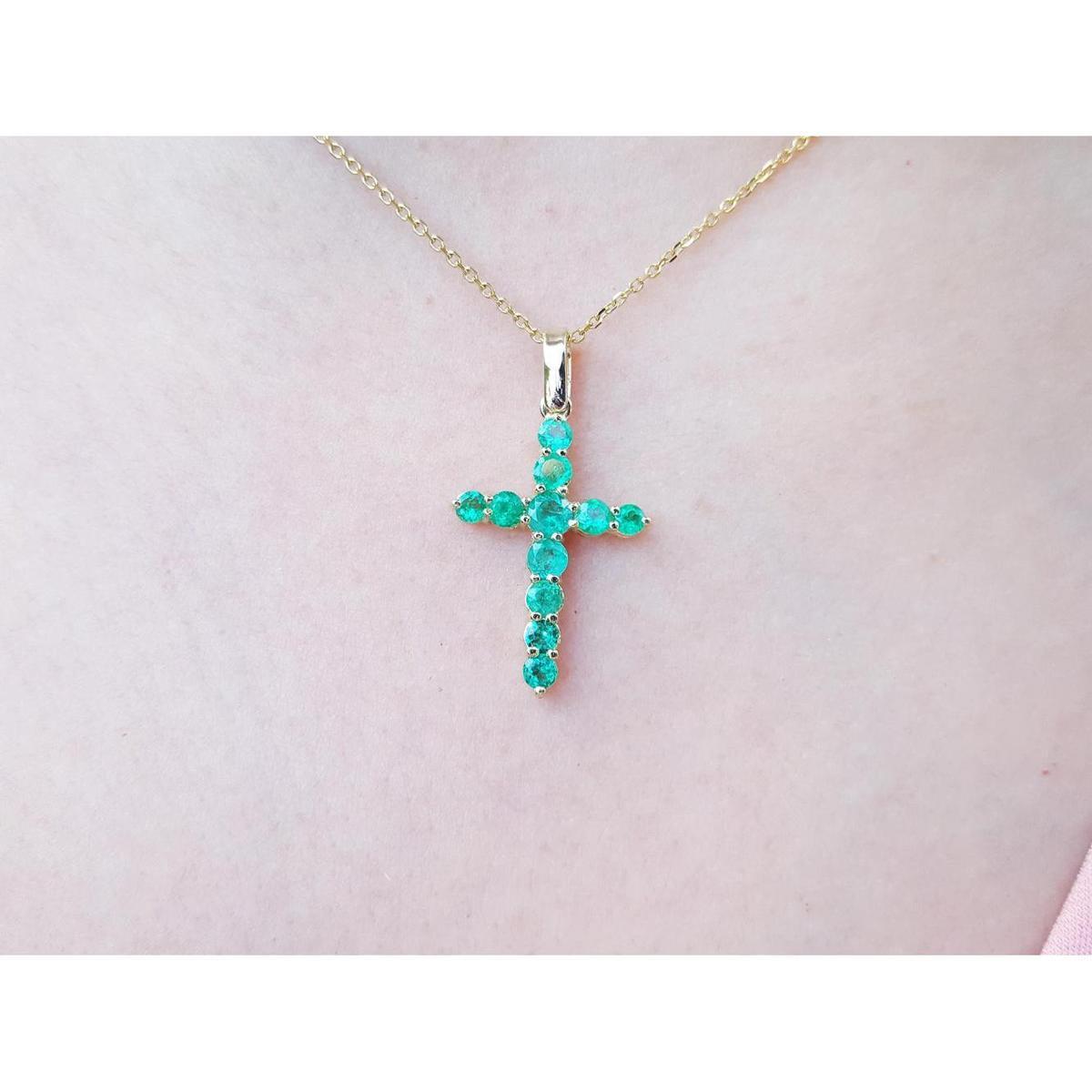 Gold cross necklace with genuine emeralds on a person's neck.