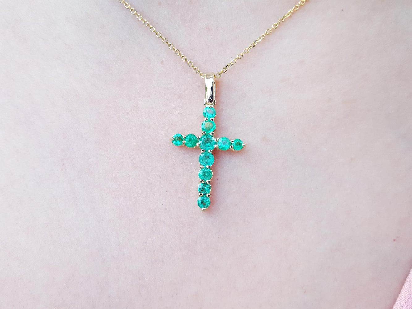 Gold cross necklace with genuine emeralds on a person&#39;s neck.