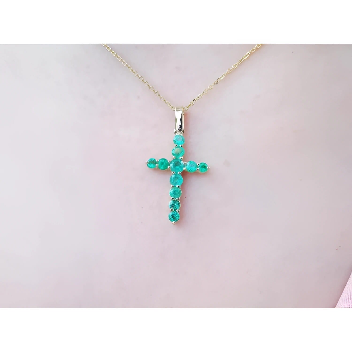 18K yellow gold cross pendant with genuine emeralds on a delicate chain, worn on a person.