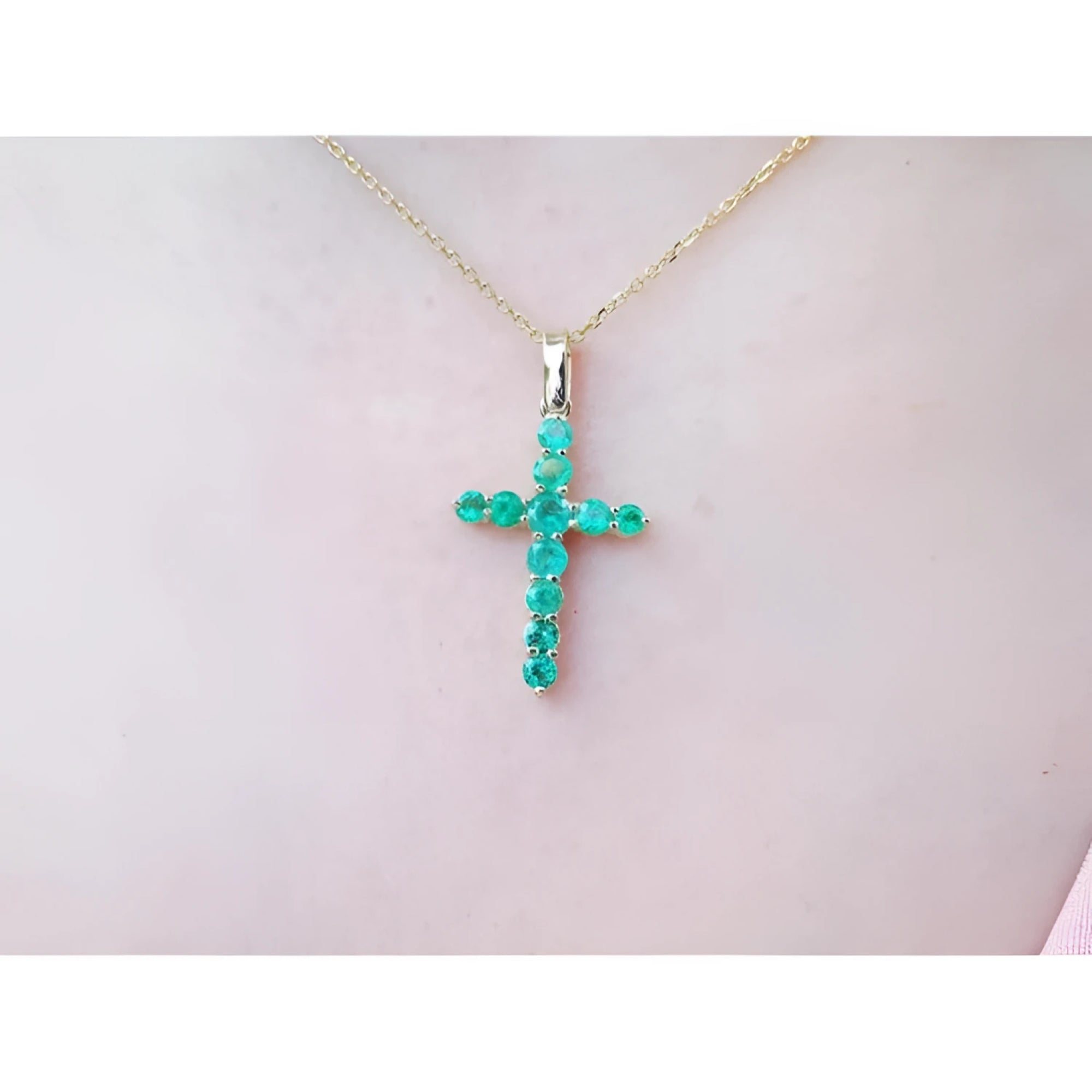 18K yellow gold cross pendant with genuine emeralds on a delicate chain, worn on a person.