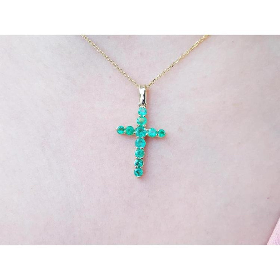 18K yellow gold cross pendant with genuine emeralds on a delicate chain, worn on a person.