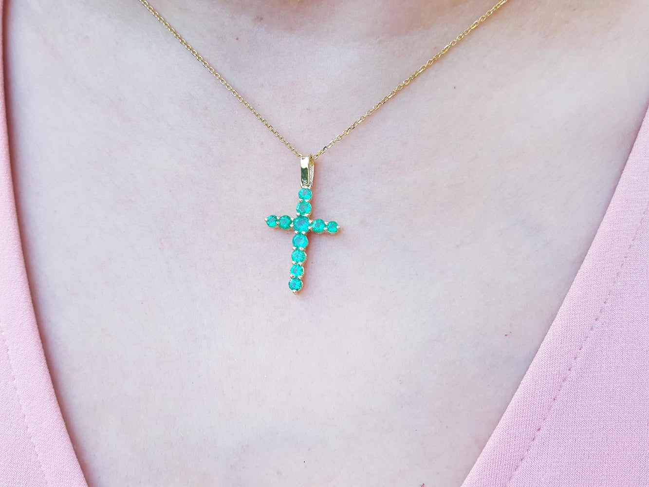 Gold necklace with a natural emerald cross pendant on a person wearing a pink top.