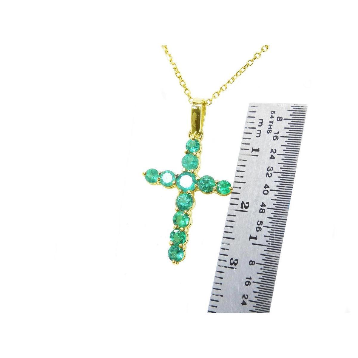 Gold cross pendant with round cut natural colombian emeralds  next to a ruler for scale on a white background.