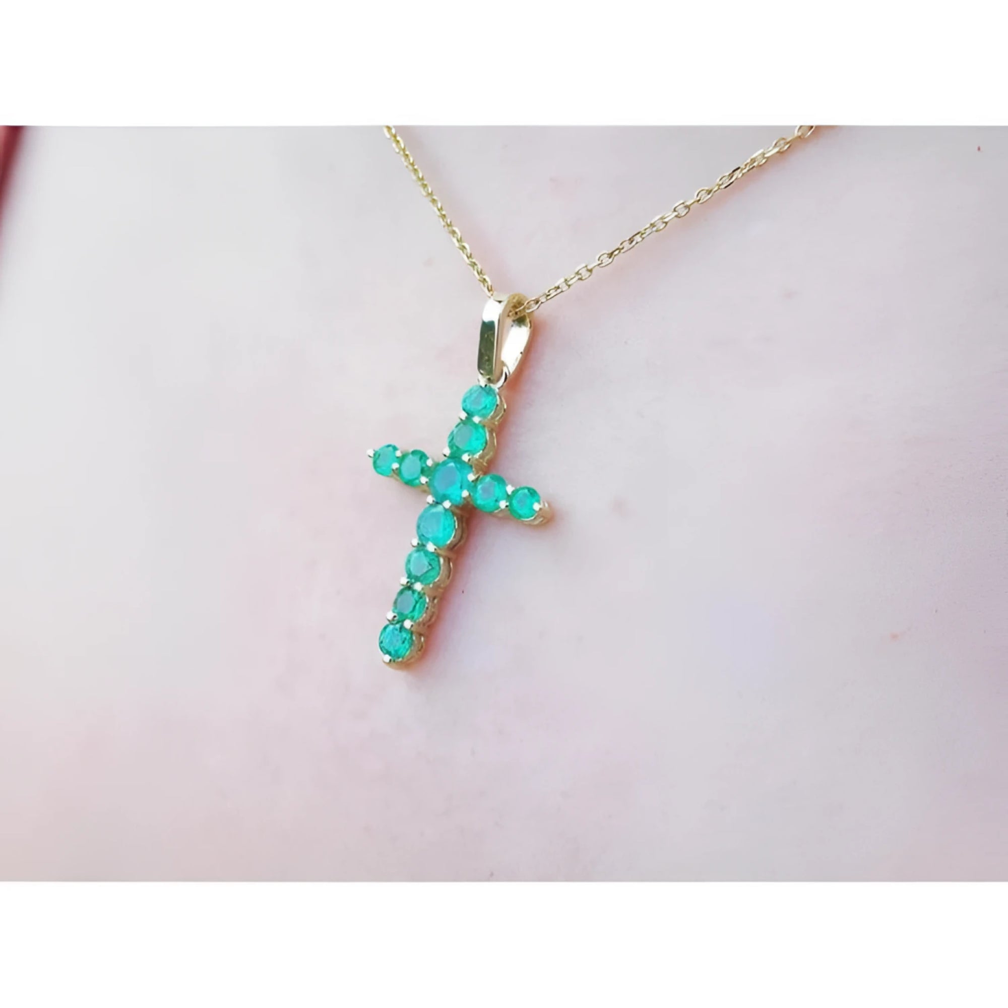 Yellow gold emerald cross pendant on a light pink skin background.