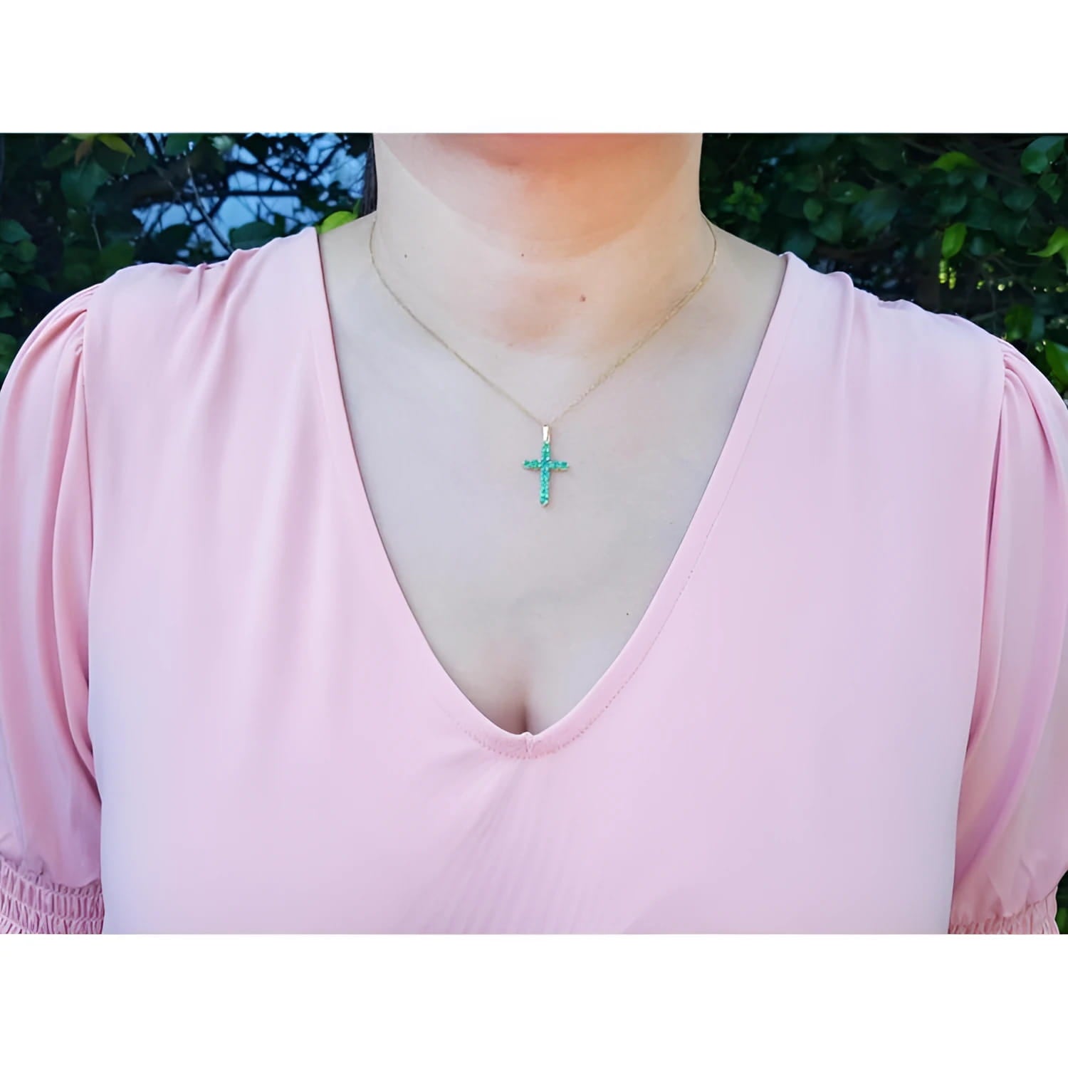 18K yellow gold necklace with a vibrant green emerald cross pendant on a woman's chest.