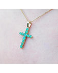 Yellow gold emerald cross pendant on a light pink skin background.