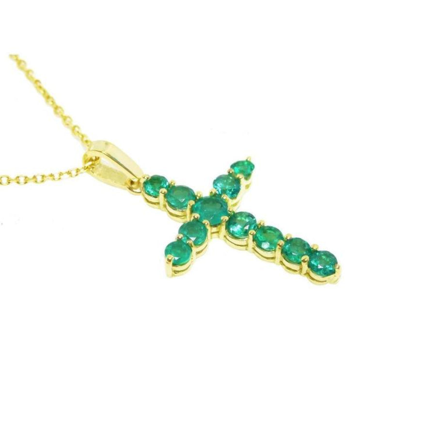 A 18k yellow gold emerald cross pendant necklace displaying 11 round cut colombian emeralds prong set.