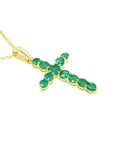 A 18k yellow gold emerald cross pendant necklace displaying 11 round cut colombian emeralds prong set.