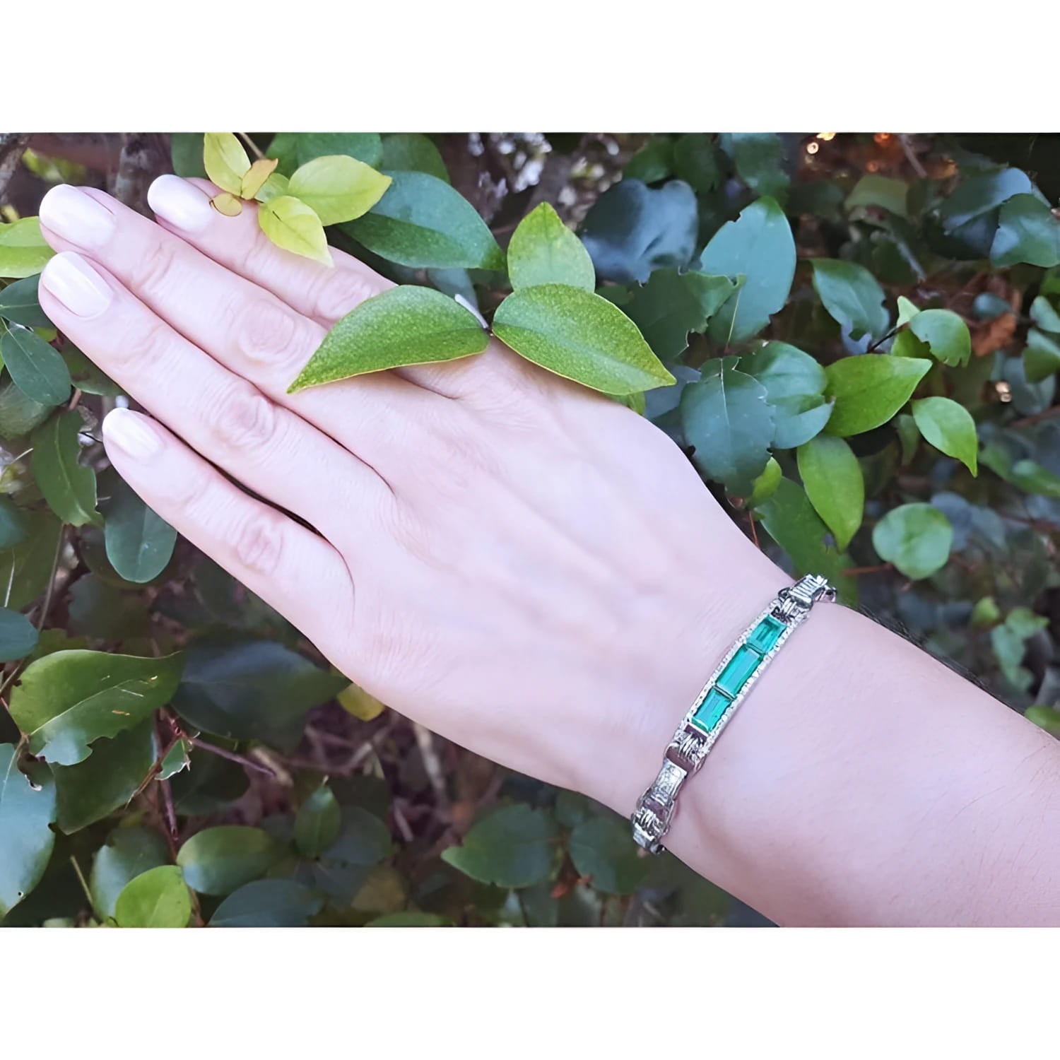 Silver bracelet with vibrant Colombian emeralds and princess-cut diamonds on a woman's wrist.