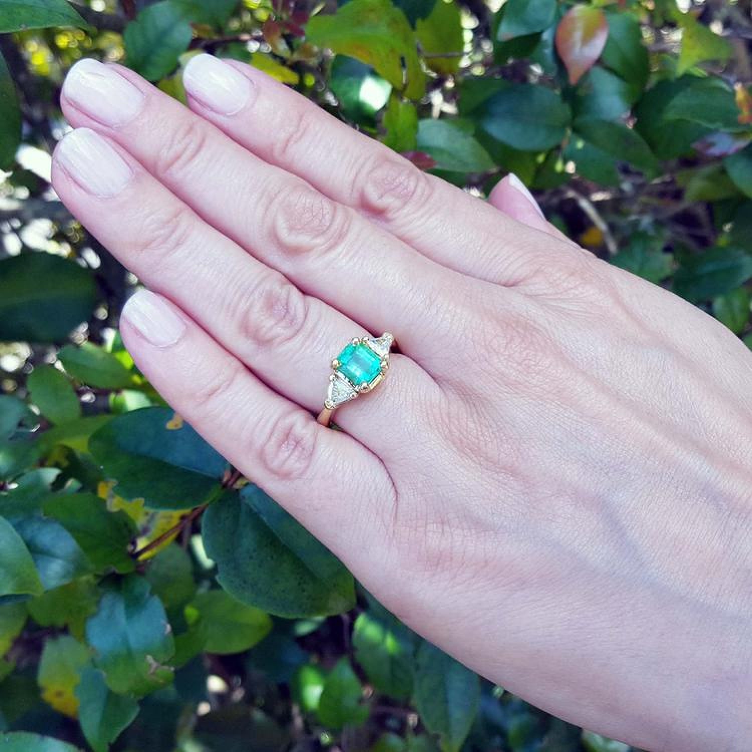 1.51 ct. emerald and trillion cut diamonds ring in 18k gold on a hand.