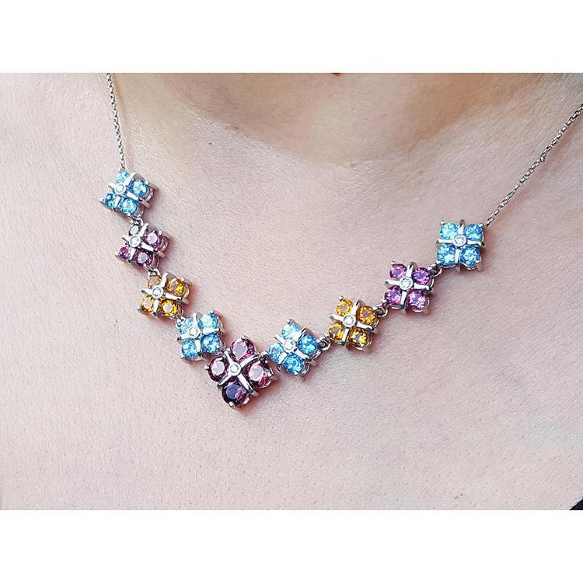 18K white gold necklace with tri-colored topaz X-cluster links on a model's neck.