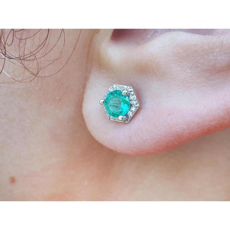 A geometric hexagonal emerald stud earrings with halo diamond worn on an earlobe.