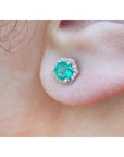 A geometric hexagonal emerald stud earrings with halo diamond worn on an earlobe.