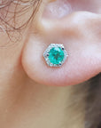 Close-up of an earlobe wearing an hexagonal halo diamond emerald stud earring.