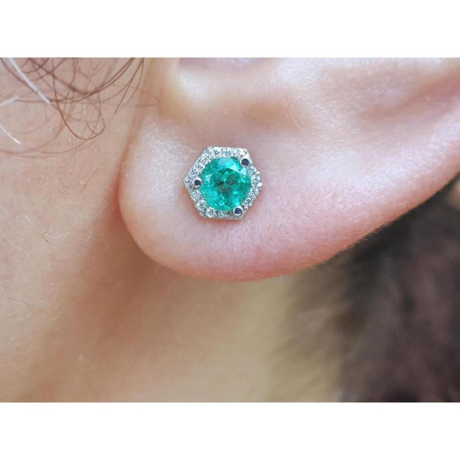 Round cut emerald stud earring in 14K white gold with hexagonal diamond halo on an ear.