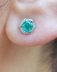 A very close-up of an earlobe dressing an emerald stud earring with hexagonal halo diamond.