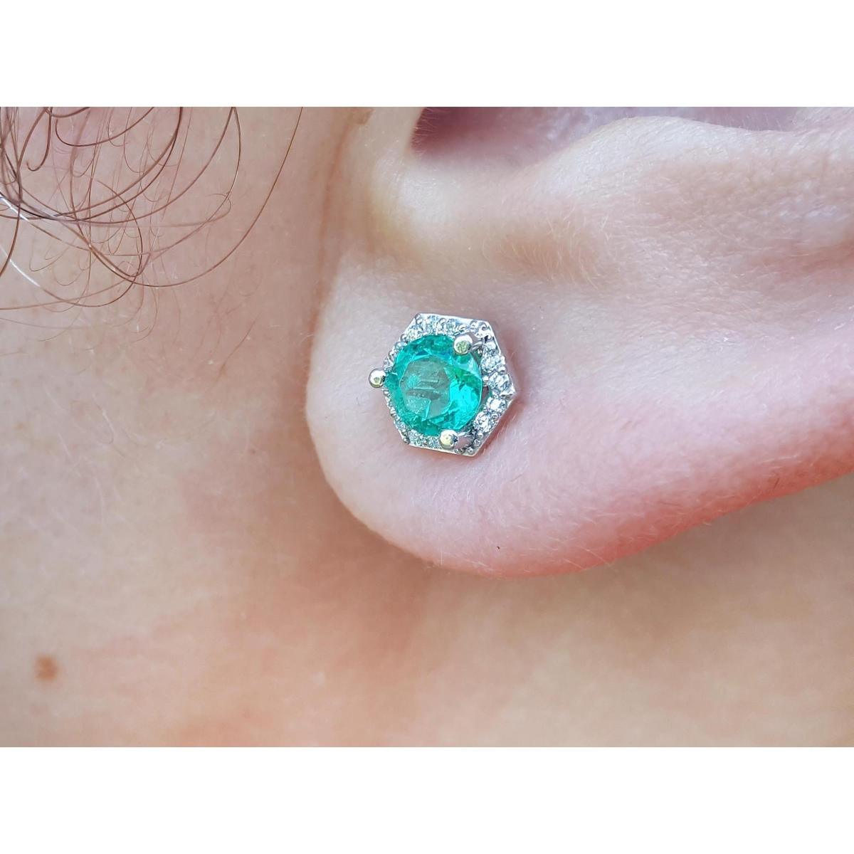 A geometri hexagonal emerald stud earrings with halo diamond worn on an earlobe close-up view.
