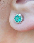 A geometri hexagonal emerald stud earrings with halo diamond worn on an earlobe close-up view.