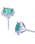 A pair of emerald stud earrings hexagonal halo diamonds, underside profile view.