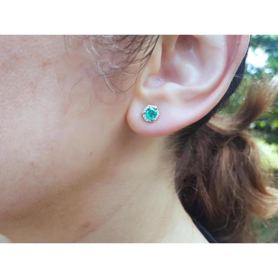 Emerald stud earring with hexagonal diamond halo in 14K white gold on an ear.