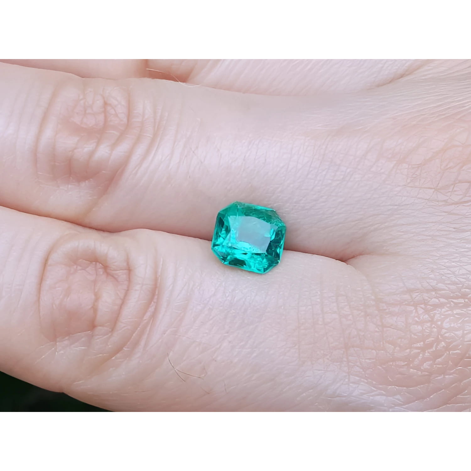 2.45 ct. GIA certified Asscher cut emerald with vibrant bluish-green color on a person's hand.