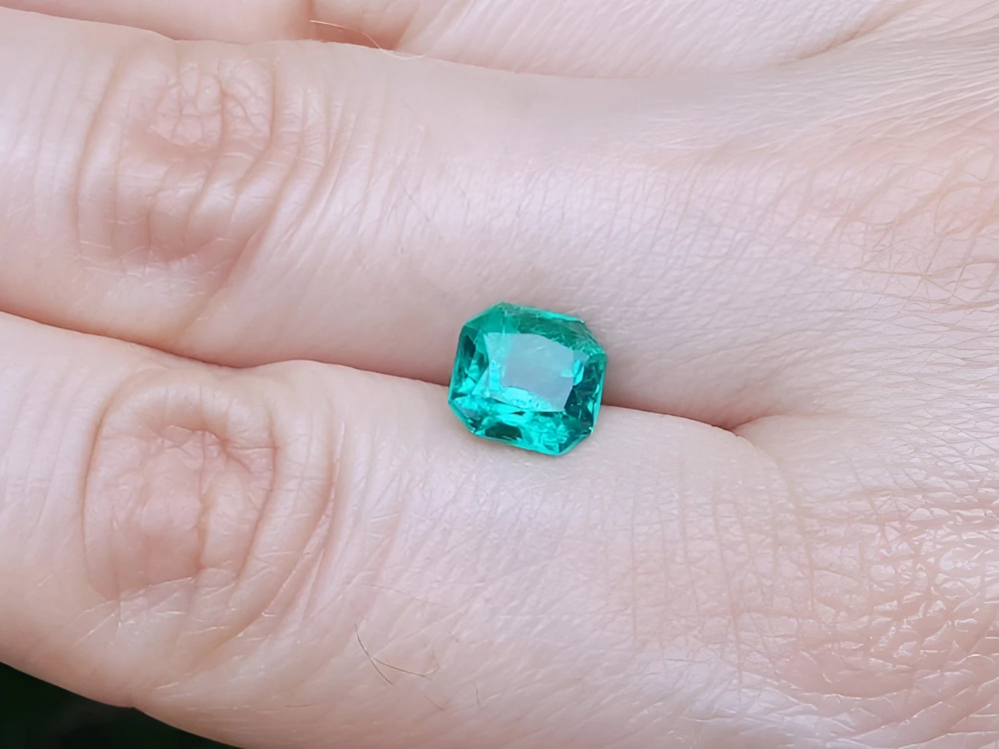 2.45 ct. GIA certified Asscher cut emerald with vibrant bluish-green color on a person's hand.