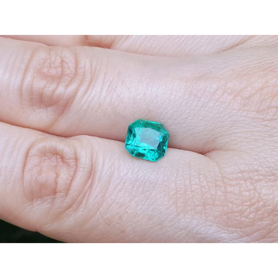 2.45 ct. GIA certified Asscher cut emerald with vibrant bluish-green color on a person's hand.