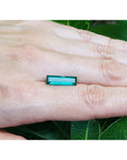 3.13 carat baguette cut Colombian emerald, eye clean, sparkling bluish-green, held on a hand with green leaves in the background.