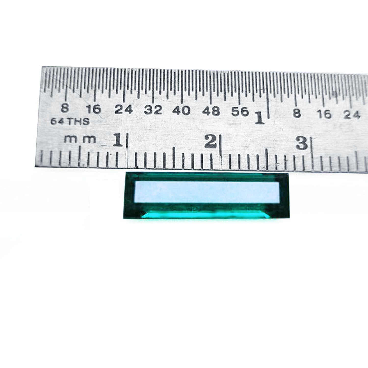 Baguette cut Colombian emerald, sparkling bluish-green, shown with a ruler for scale.