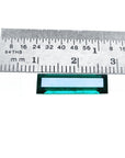 Baguette cut Colombian emerald, sparkling bluish-green, shown with a ruler for scale.
