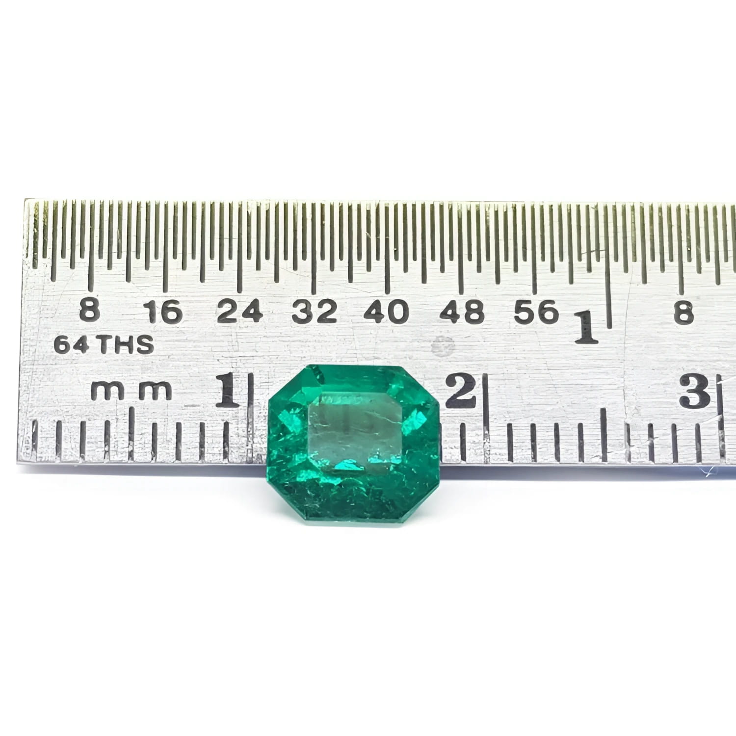 GIA certified 1.40 carat emerald-cut Colombian emerald with sparkling bluish-green color, next to a ruler.