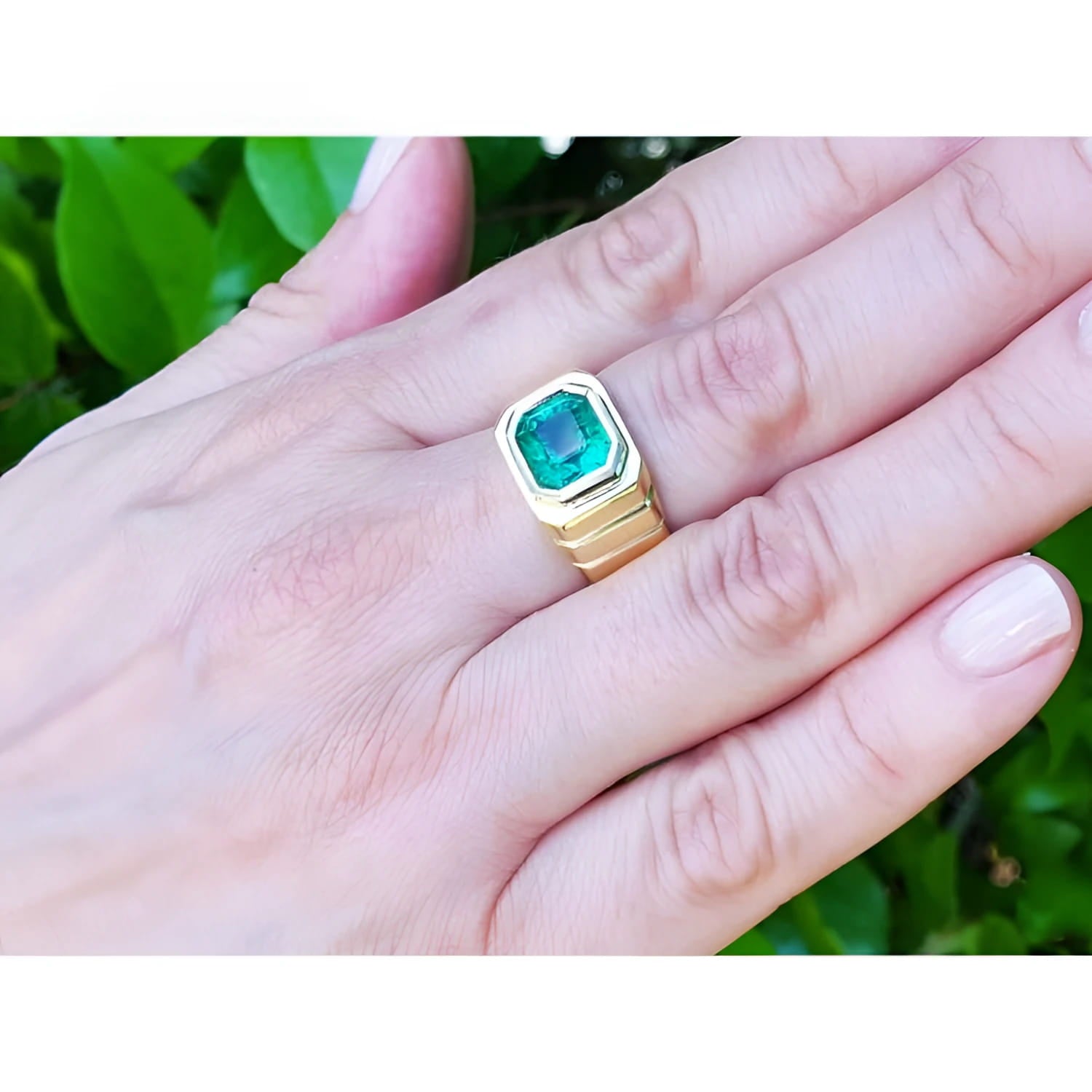 Men's 18K yellow gold ring with a medium-deep green emerald in a full bezel setting, worn on a hand.