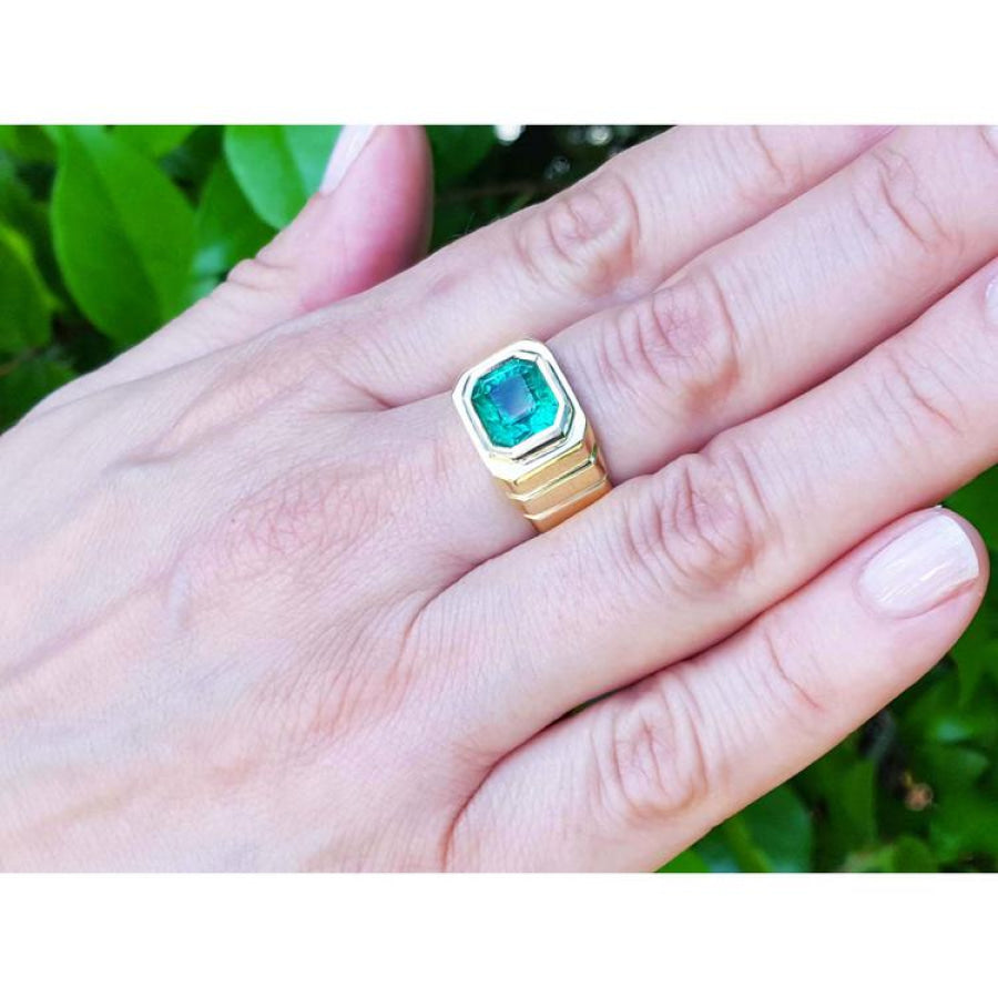 Men's 18K yellow gold ring with a medium-deep green emerald in a full bezel setting, worn on a hand.