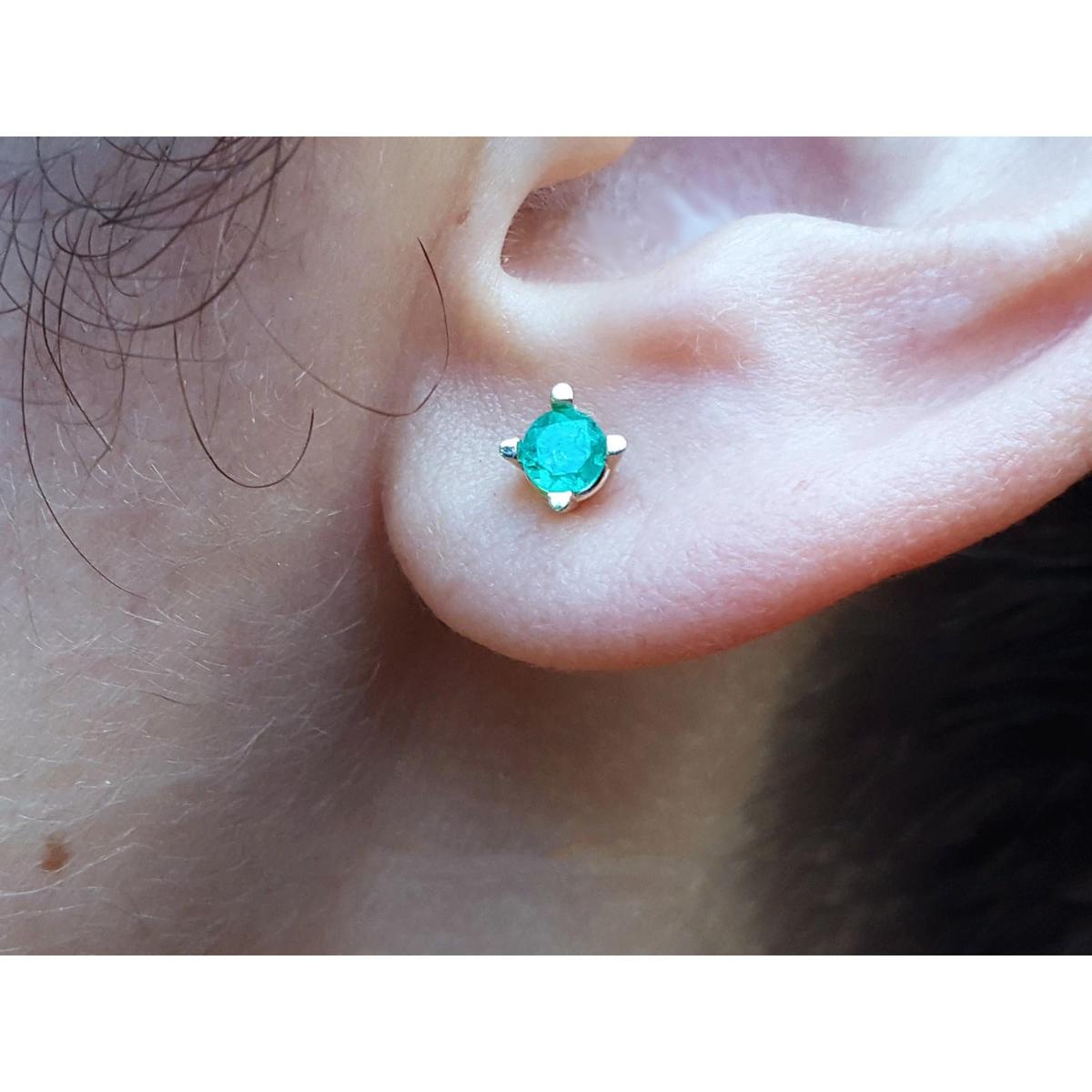 Close-up of an ear wearing a emerald stud earring with a blurred natural background.