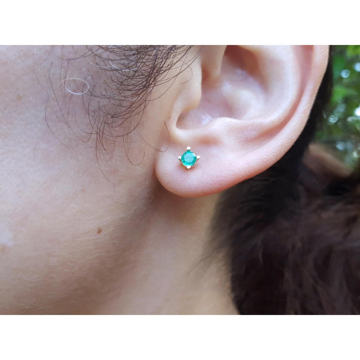 Close-up of an ear wearing a emerald stud earring with a blurred natural background.