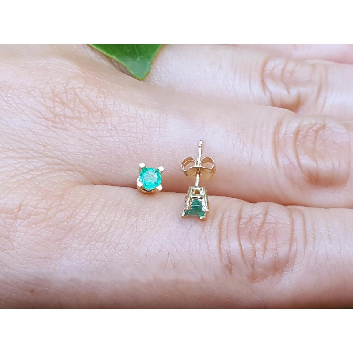Gold earrings with round cut emeralds gemstones on a person's finger