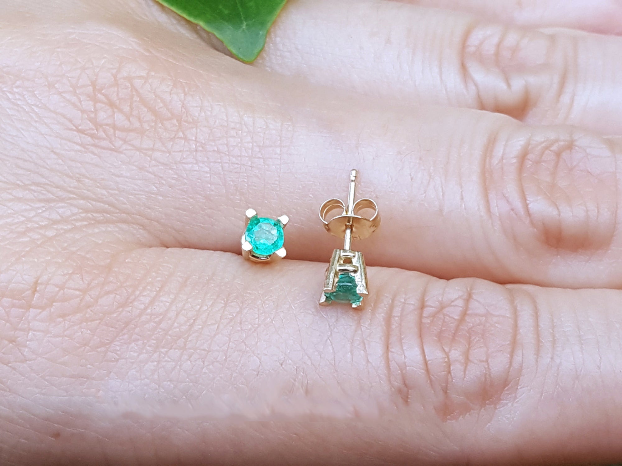 Gold earrings with round cut emeralds gemstones on a person&#39;s finger