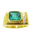 A yellow gold ring with a natural emerald bezel set and small diamonds on a topside view.