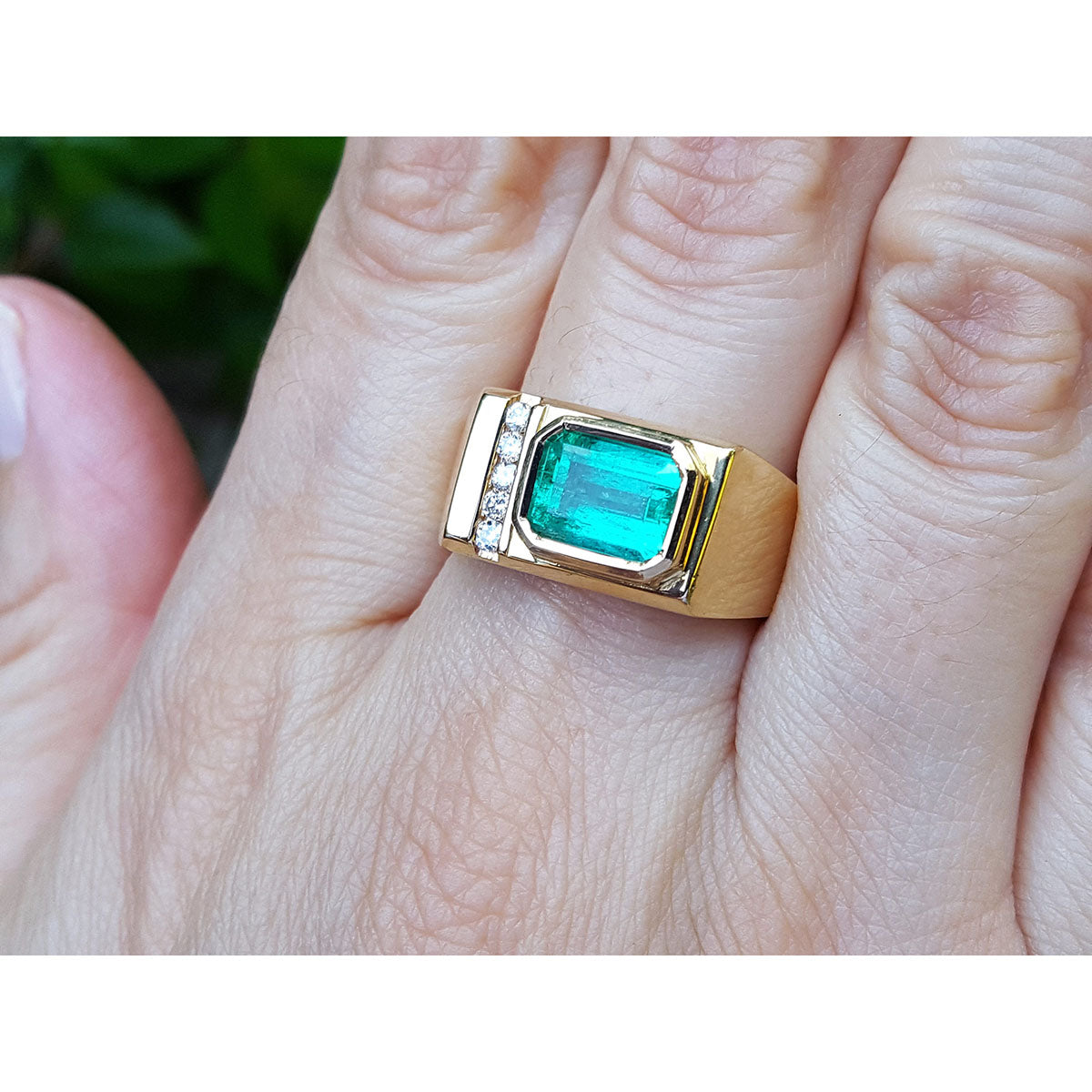 Gold mens ring with a bezel set emerald on a hand.