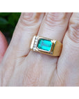 Gold mens ring with a bezel set emerald on a hand.
