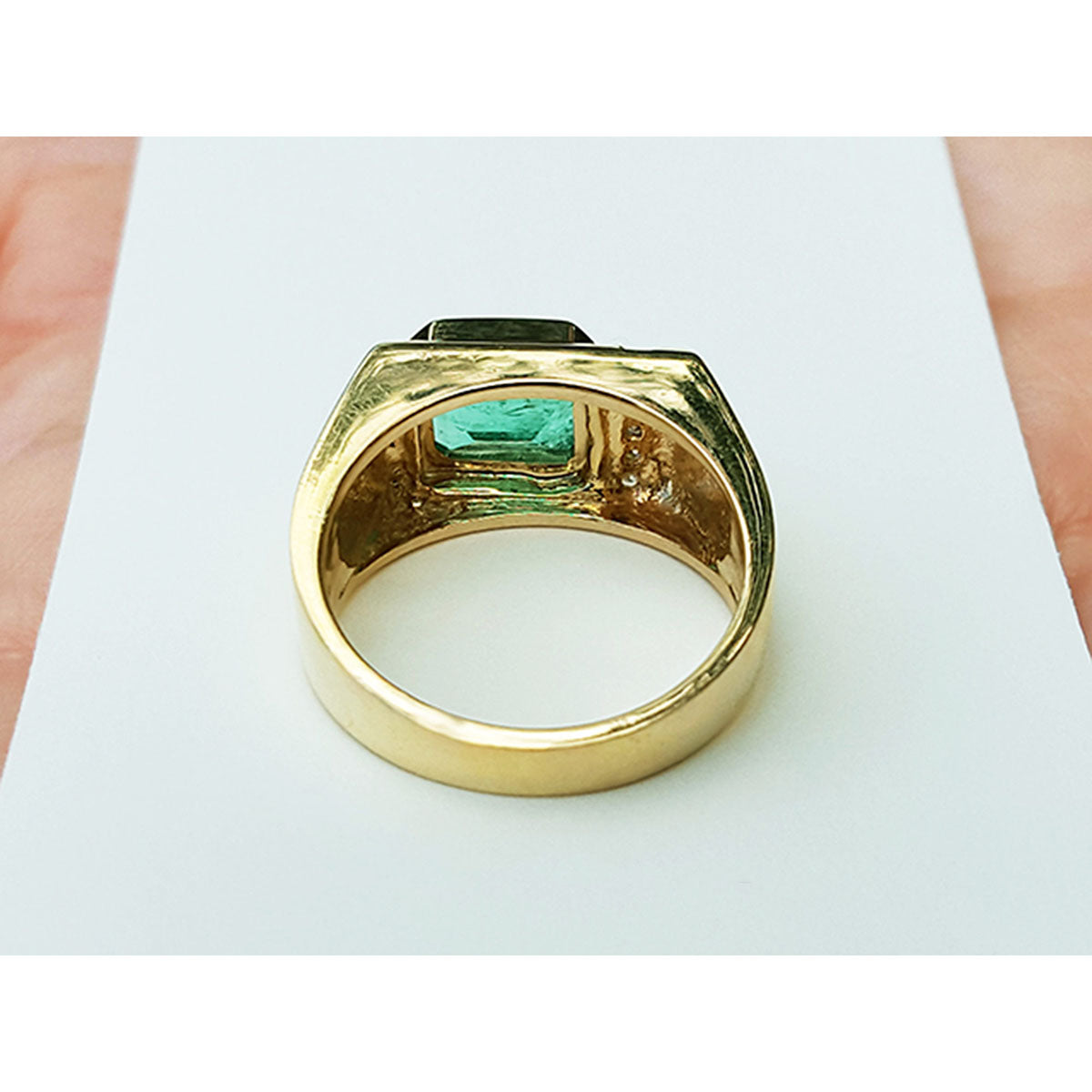 The underside view of a yellow gold men&#39;s emerald ring on a white background.