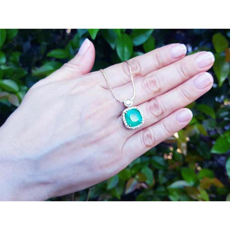 Hand wearing a gold natural emerald necklace cushion cut 8.07 carats encircled in a halo of natural diamond
