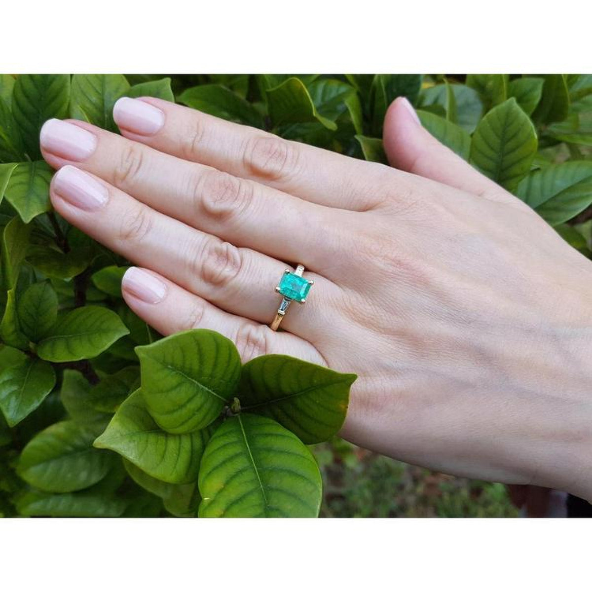 14K gold ring with a rectangular emerald-cut emerald and tapered baguette side diamonds on a hand.